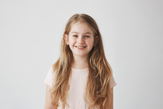 Close up of funny little girl with blue eyes and blonde hair laughing,looking in camera with satisfied expression, posing for family photo.