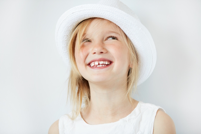 Close up portrait of adorable blonde little girl wearing white hat, laughing and having fun indoor. Cute 5-year old female smiling and showing her teeth. Isolated portrait of beautiful Caucasian child